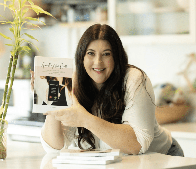 a woman smiling holding a book in a soft-coloured kitchen